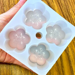 May include: White silicone mold with four flower-shaped cavities. The mold is designed to create small cakes or other treats.