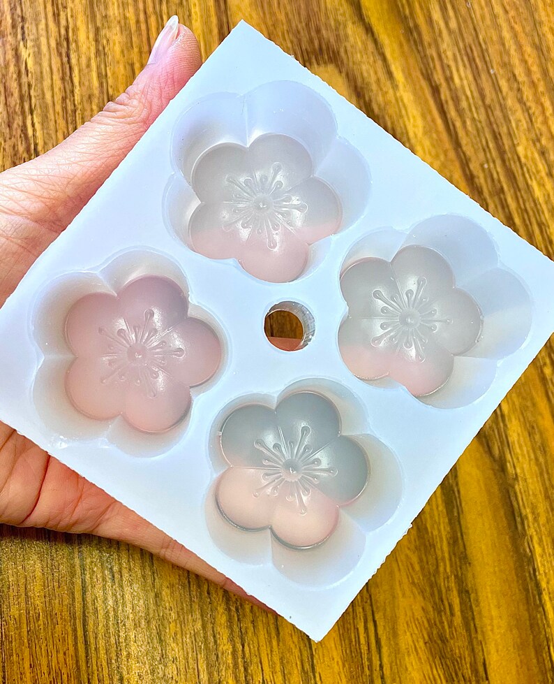 May include: White silicone mold with four flower-shaped cavities. The mold is designed to create small cakes or other treats.