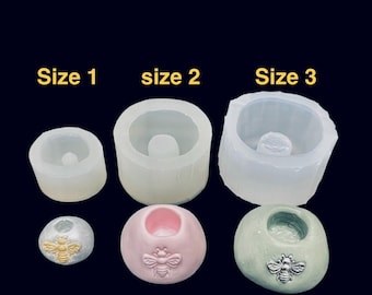 May include: Three translucent silicone molds labeled Size 1, size 2, and Size 3, paired with three finished circular objects in light blue, pink, and sage green, each featuring a small embossed bee emblem on the front surface.