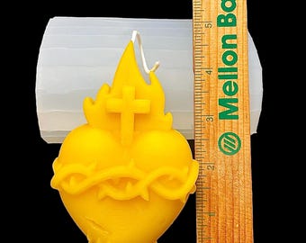 May include: A yellow wax candle shaped like a heart with a cross and a crown of thorns. The candle is about 4 inches tall and is next to a ruler.