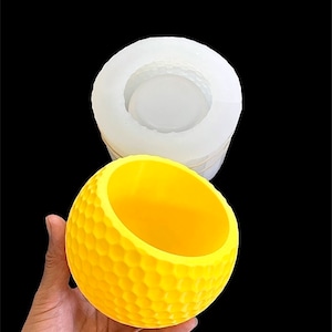 Könnte beinhalten: Eine gelbe, runde Silikonform mit einem Wabenmuster. Die Form ist für die Herstellung eines dekorativen Pflanzgefäßes oder einer Schale konzipiert.