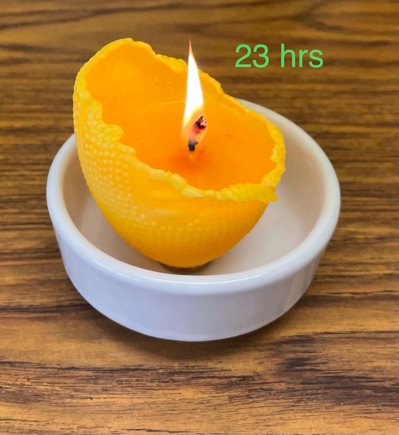 K&ouml;nnte beinhalten: Eine gelbe Zitruskerze brennt in einer wei&szlig;en Schale. Die Kerze hat eine strukturierte Oberfl&auml;che und ist mit "23 Stunden" beschriftet.