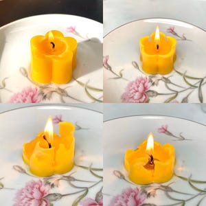 May include: Four yellow flower-shaped candles, two are lit and two are unlit. The candles are on white plates with floral designs.