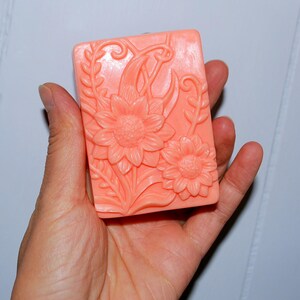 May include: A peach-colored soap bar with a floral design featuring sunflowers and leaves.