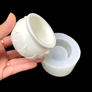 Könnte beinhalten: Weiße Silikonform zum Herstellen eines kleinen Dekotopfes mit einem erhabenen Design. Die Form besteht aus zwei Teilen, einem für den oberen und einem für den unteren Teil.
