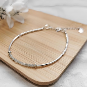 May include: A silver bracelet with a delicate chain and small, clear stones. The bracelet is on a wooden surface.