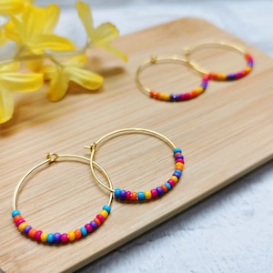 May include: A pair of gold hoop earrings with colorful beads. The beads are arranged in a rainbow pattern, with purple, orange, yellow, and blue beads.