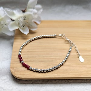 Peut inclure: Un bracelet en argent avec des perles et une rangée de perles de pierres précieuses rouges.