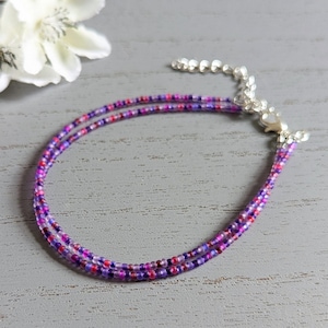 May include: A delicate anklet made with tiny purple, pink, and red beads. The anklet has a silver clasp.