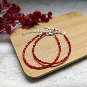 May include: Two red beaded bracelets with silver clasps on a wooden surface.