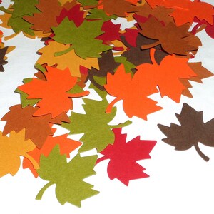 May include: A collection of maple leaf cutouts in various fall colors, including orange, brown, green, and red. These decorative leaves are scattered across a white surface, perfect for autumn-themed crafts and decorations.