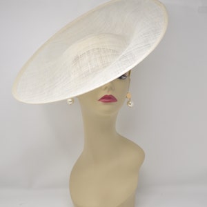 May include: A large, off-white, wide-brimmed hat made of woven straw. The hat is tilted at an angle, and the brim is curved upwards.