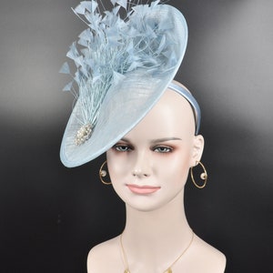 May include: A light blue fascinator hat with a large, round brim and a cluster of feathers on top. The hat is decorated with a small, sparkly embellishment.