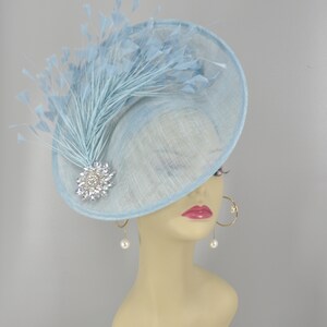 May include: A light blue hat with a large brim and a feather accent. The hat is decorated with a sparkly brooch.
