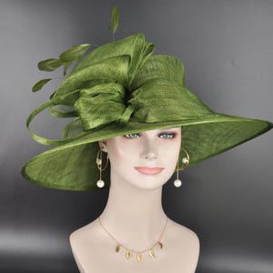 May include: An olive green wide-brimmed hat featuring a structured crown and a large, layered bow detail on the side. The hat is adorned with delicate green feathers extending from the top. The material has a visible woven texture throughout.