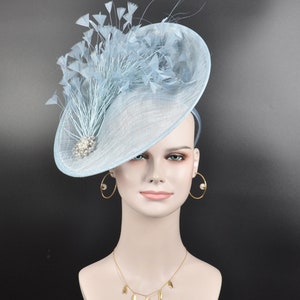 May include: A light blue fascinator hat with a large, wide brim and a cluster of feathers on top. The hat is decorated with a small, sparkly brooch.