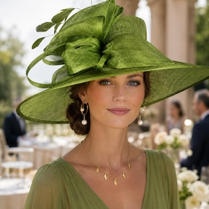May include: A wide-brimmed grass green hat featuring a large structured bow and leaf accents on the side. The ensemble includes gold hoop earrings with dangling white pearls and a delicate gold necklace with small leaf-shaped charms.