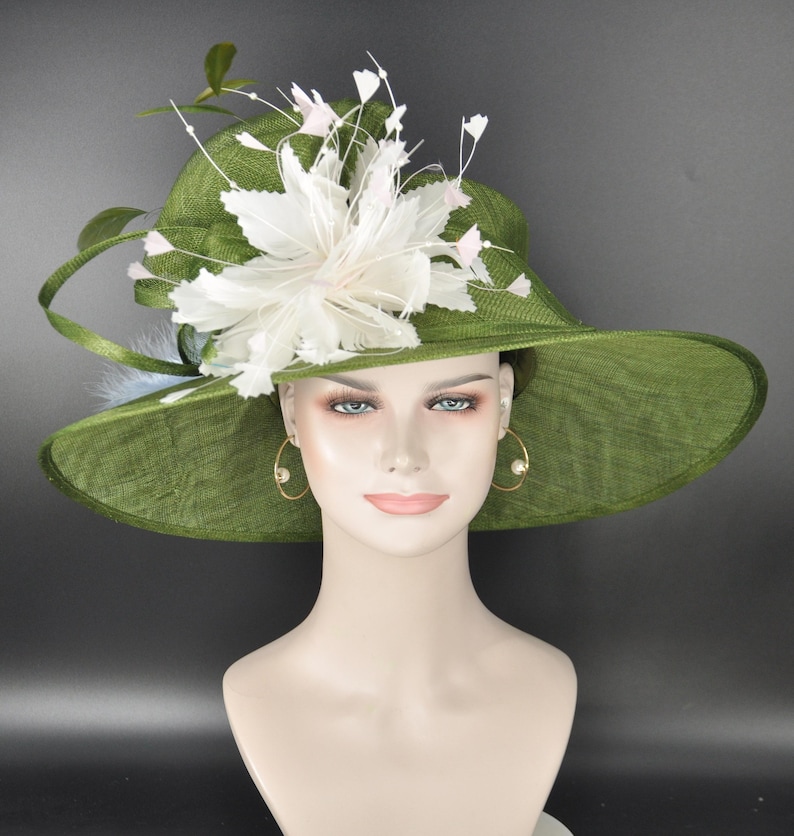 May include: A wide-brimmed olive green hat featuring a textured woven finish. The hat is adorned with a large, layered white floral embellishment made of feathers and delicate stems, positioned asymmetrically on the side of the crown.