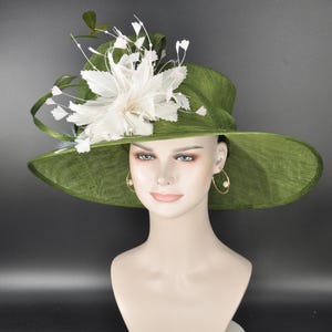 May include: A wide-brimmed olive green hat featuring a textured fabric finish. The hat is adorned with a large, layered white floral embellishment made of delicate petals and thin, wispy stems that extend outward from the side of the crown.