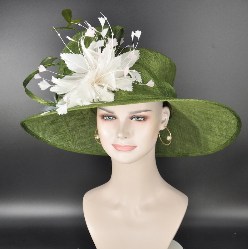 May include: A wide-brimmed olive green hat featuring a textured fabric finish. The hat is adorned with a large, layered white floral embellishment made of delicate petals and thin, wispy stems that extend outward from the side of the crown.