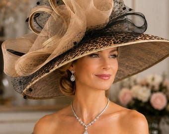 May include: A wide-brimmed hat featuring a leopard print pattern on the underside of the brim. The top is adorned with large, structured beige fabric loops and black netting with small black dots. The hat has a wide, flat, circular brim.
