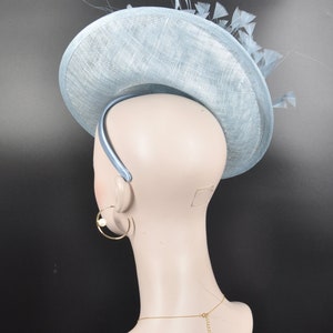 May include: A light blue hat with a wide brim and feathers. The hat is made of a straw-like material and has a headband.