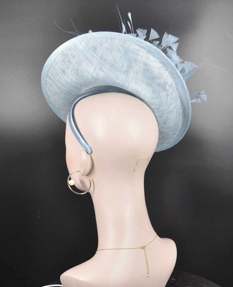 May include: A light blue hat with a wide brim and feathers. The hat is made of a straw-like material and has a headband.
