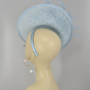 May include: A light blue hat with a wide brim and a feather detail. The hat is made of a straw-like material and has a headband.
