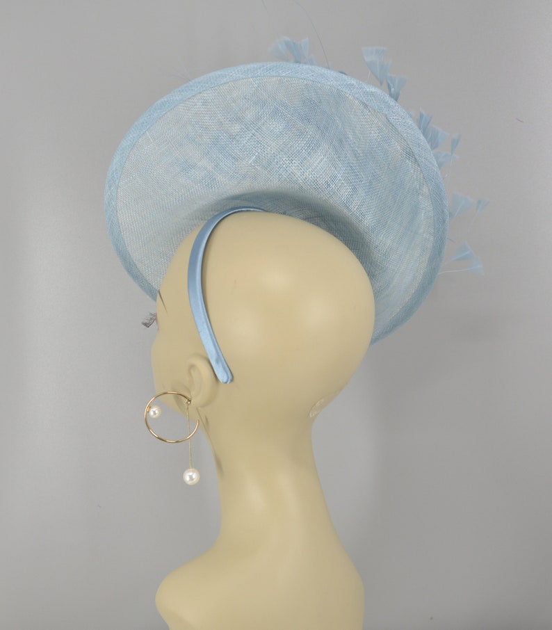 May include: A light blue hat with a wide brim and a feather detail. The hat is made of a straw-like material and has a headband.