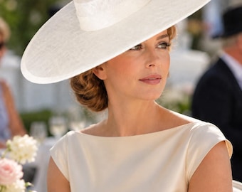 May include: A wide-brimmed white hat with a flat crown and a smooth, textured finish. The hat features a structured, circular brim and a matching band around the base of the crown, providing a clean, solid white appearance throughout the design.