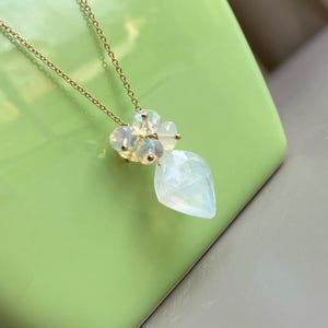 May include: A gold chain necklace with a pendant featuring a large, teardrop-shaped white gemstone and smaller white gemstones clustered around it.