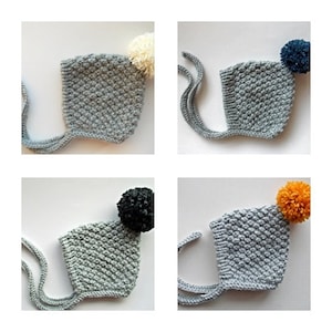 May include: Four grey knitted baby hats with different coloured pom-poms. The hats have a tie at the back.
