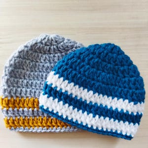 May include: Two crocheted hats, one gray with a yellow stripe and one blue with white stripes.