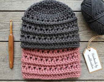 Puede incluir: Un gorro de ganchillo hecho a mano en dos tonos: gris y rosa empolvado. El gorro está hecho con un patrón de puntada texturizada. Un ganchillo de madera y una madeja de hilo gris están junto al gorro. Una etiqueta que dice "Handmade by candlcreation" está adjunta.