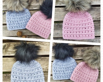 May include: Four crocheted hats with faux fur pom poms. Two hats are light blue and two hats are pink. The pom poms are black and brown.