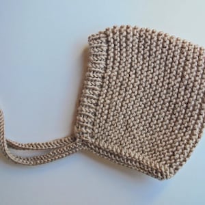 Puede incluir: Un gorro de bebé de punto beige con una cuerda atada.
