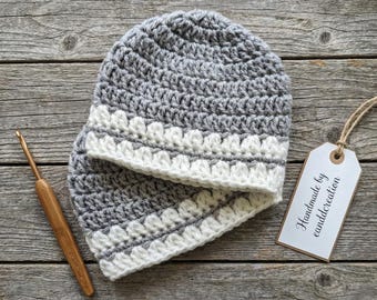 May include: Two crocheted beanies in gray and white, with a crochet hook and a tag that says "Handmade by canddcreation". The beanies are made of a soft yarn and have a textured design. The tag is attached with a string.