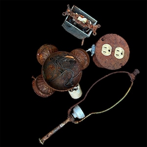 May include: A collection of weathered electrical components including a rectangular wall switch, a circular dual-outlet wall plate, a rusted metal lamp base with internal wiring, and a metal lamp harp, all showing significant oxidation and rust.