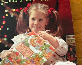 May include: A young girl with pigtails and red bows holds a Christmas-themed gift. The gift is wrapped in colorful paper with teddy bears, stockings, and the words "Joyeux Noel". The background includes the text "Current, Inc."