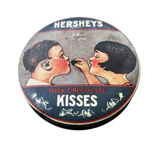May include: Vintage Hershey's Kisses tin with a circular design. The tin features a boy and girl sharing a kiss, with the words "Hershey's" and "Milk Chocolate Kisses" prominently displayed. The phrase "A Kiss for you" is also included.