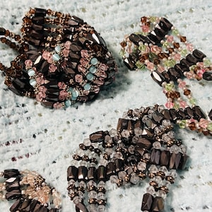 May include: Three multi-strand bracelets constructed from dark metallic hematite-style beads interspersed with smaller faceted crystal beads in shades of pink, light blue, clear, and pale green, arranged in intricate, layered, woven patterns.