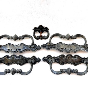 May include: Antique bronze-toned drawer pulls and a matching knob. The pulls have a decorative, ornate design with curved handles and a central embellishment. The knob is smaller, with a similar design. Ideal for vintage furniture restoration.