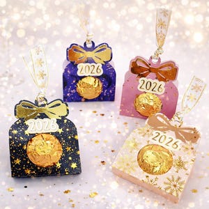 May include: Four decorative gift boxes in navy, pink, and gold, each with a bow and the year "2026" printed on them. The boxes have a gold-coloured sweet inside and are decorated with stars and snowflakes. Ribbons with snowflake patterns are attached.