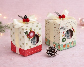 May include: Two festive Christmas gift boxes, each adorned with cream ribbons and red berry decorations. The boxes feature patterned designs, a red polka dot base, and a circular window. One box has a "Merry Xmas" tag.