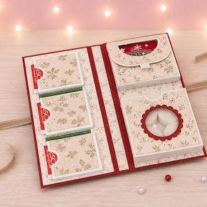 May include: Open Christmas-themed gift card holder with a floral pattern and red accents. The holder has multiple compartments, including a windowed section with white objects. A ribbon is attached for closure.