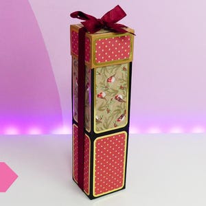 May include: A tall, red and gold gift box with a red bow and a polka dot pattern. The box is decorated with a floral design and small birds. The text "ESEMPIO" is visible in the lower left corner of the image.