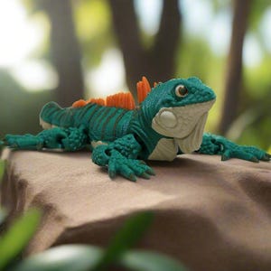 May include: A detailed, teal-colored toy iguana with orange spines and a cream-colored underbelly rests on a rock. The iguana has a detailed, textured skin and is set against a blurred, natural background of green foliage.