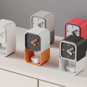 May include: A collection of modern, minimalist clocks in various colors. The clocks have a square face with a simple arrow-shaped hand. Colors include white, gray, orange, red, and black. Each clock has a small, white, rounded object at the base.