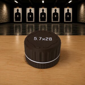 May include: A cylindrical black thread protector with a textured grip and a thin white ring around the base. The top surface features the white text 5.7x28, indicating the caliber. The object has a matte finish and a grooved side profile.