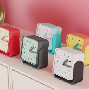May include: A collection of five colorful square analog clocks. Each clock features a different color scheme: red, gray, blue, yellow, and white. The clocks have a minimalist design with a square face and a curved base.